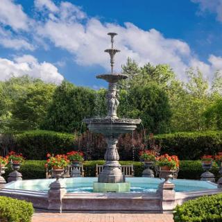 A beautiful fountain surrounded by lush gardens and hedges under a clear blue sky.