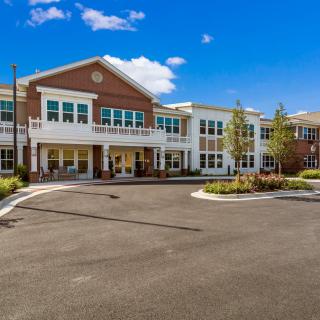 A modern residential building with a large parking lot and landscaped surroundings under a bright blue sky.