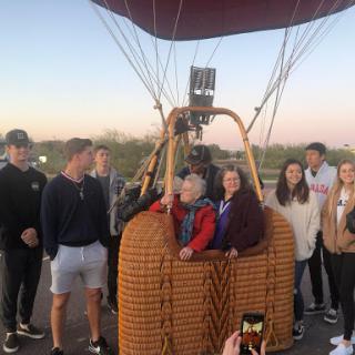 A group of people gathered around a hot air balloon, preparing for an exciting adventure as the sun sets.