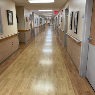 A view of a well-lit hospital corridor featuring wooden flooring and framed artwork along the walls.