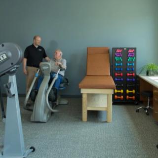 A therapist assists a patient using exercise equipment in a rehabilitation room.