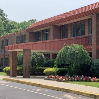 A two-story brick building with a landscaped entrance featuring trees and flowers.