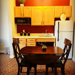 A cozy kitchen and dining area with a wooden table and chairs, featuring light wood cabinets and a refrigerator.
