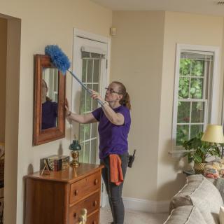 A person cleaning a mirror in the living room using a duster.