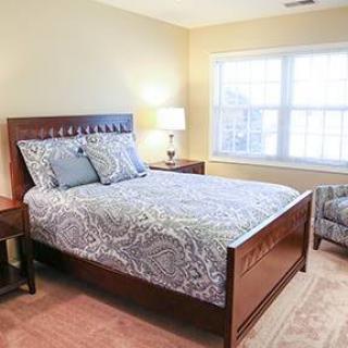 A cozy bedroom featuring a wooden bed with patterned bedding, a bedside lamp, and a large window letting in natural light.