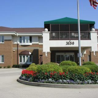A two-story building with a garden in front and a flagpole standing on the driveway.