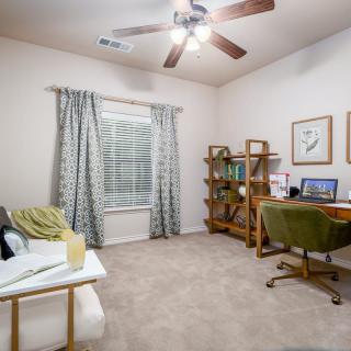 A cozy home office with a desk, chair, bookshelf, and window with curtains.