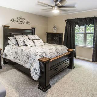A well-decorated bedroom featuring a large bed with a patterned comforter, dark wooden furniture, and a ceiling fan.
