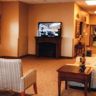 A cozy living room with a television mounted above a fireplace, surrounded by comfortable seating and warm lighting.