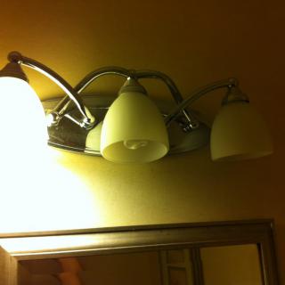 Bathroom light fixture with three bulbs above a mirror.