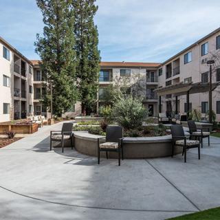 A modern apartment complex courtyard with outdoor seating and landscaping.