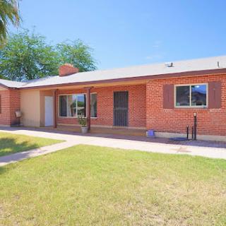 A charming single-story brick house with a well-maintained front yard under a clear blue sky.