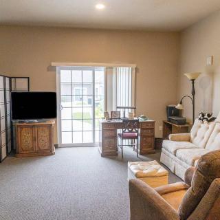 A cozy living room with a sofa, desk, and television, featuring large windows that let in natural light.