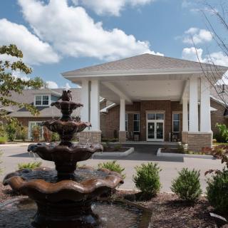 A building entrance with a decorative fountain in the foreground under a partly cloudy sky.