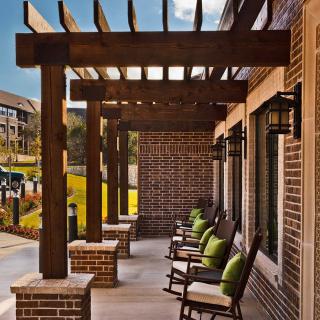 A brick patio with a wooden pergola and rocking chairs providing a shaded outdoor seating area.