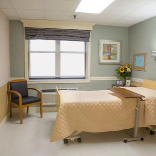 An empty hospital room with a neatly made bed and a sunny window.