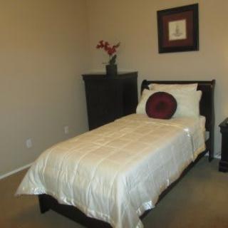 A minimalist bedroom featuring a single bed with white bedding, a decorative pillow, and framed artwork on the wall.