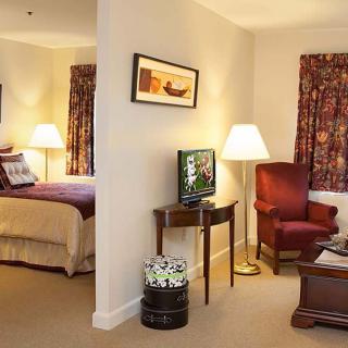 A cozy hotel room with a separate bedroom and living area, featuring traditional furniture and warm lighting.
