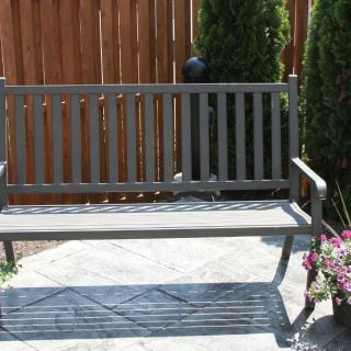 A garden bench on a patio next to potted flowers and a wooden fence.
