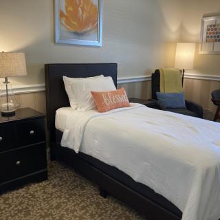 A cozy bedroom with a single bed, nightstand, and warm lighting.