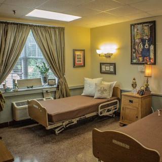 A well-lit hospital room with two patient beds, a window with curtains, and warm decor.