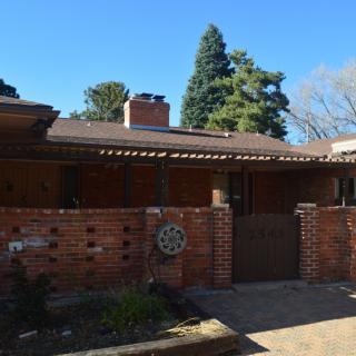 A mid-century modern brick house with a distinctive architectural design, set against a clear blue sky and surrounded by trees.