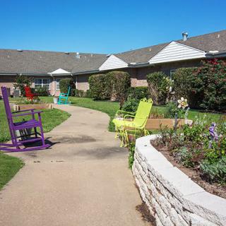 A colorful garden pathway with chairs and a building in the background on a sunny day.