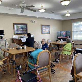 A group of seniors gathered in a community room, sitting around tables and engaging with each other.