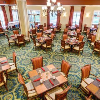 An elegant dining room with neatly arranged tables and chairs, featuring chandeliers and a carpeted floor.