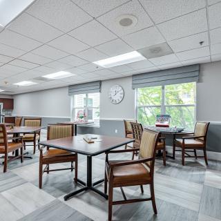 A bright and modern dining area with several tables and chairs, featuring large windows and a wall clock.