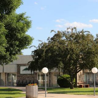 A serene view of a park area featuring a building, lush greenery, and decorative lighting.