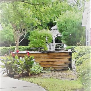 A serene garden featuring a wooden planter and a small gazebo surrounded by lush greenery.