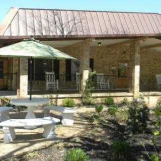 An outdoor patio area with seating, featuring a table with an umbrella and surrounded by landscaping.
