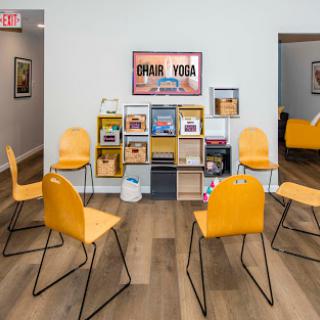 A cozy waiting area in a yoga studio featuring bright yellow chairs and an organized bookshelf.