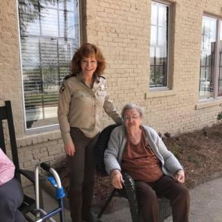 A caregiver standing next to an elderly person in a wheelchair outside a building.