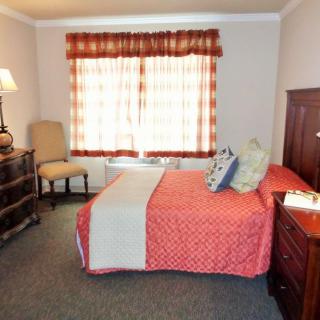 A cozy bedroom with a bed, dresser, chair, and a window with curtains.