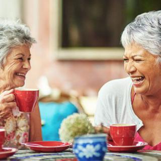 Two senior women enjoying a lively conversation over tea outdoors.