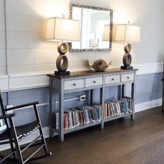 A cozy interior with a console table, lamps, mirror, and bookshelf beneath.