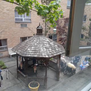 A serene view of a gazebo in a courtyard, surrounded by greenery and buildings.