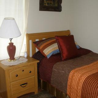 A cozy bedroom with a single bed, colorful pillows, and a lamp on the nightstand.
