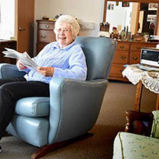 An elderly person sitting in an armchair, reading and relaxing in a cozy living room.