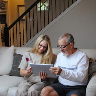 A young woman and an elderly man share a moment together, exploring a tablet in a cozy living room.