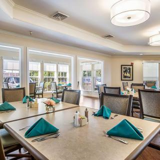 A well-lit dining room with arranged tables and teal napkins.