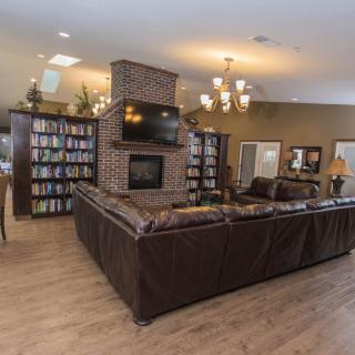 A cozy living room with a large leather sectional sofa, centered around a brick fireplace and television, flanked by bookshelves.