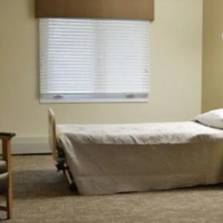 A minimalist bedroom with a single bed and a chair near a window.