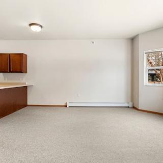 A spacious and airy open-plan living space featuring a kitchen area with wooden cabinets and ample natural light.