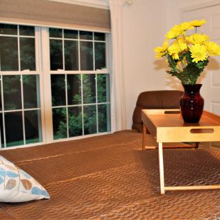 A cozy living room with a wooden table, vase of yellow flowers, and large window.