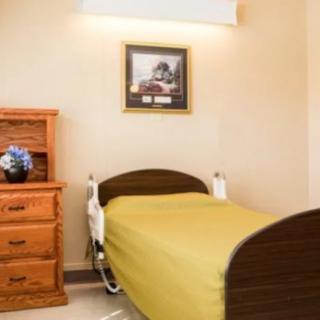 A hospital room with a single bed, wooden furniture, and decorative elements including a painting and flowers.