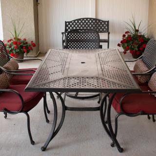 A stylish outdoor dining set featuring a decorative table and comfortable chairs with red cushions, complemented by vibrant flowers.