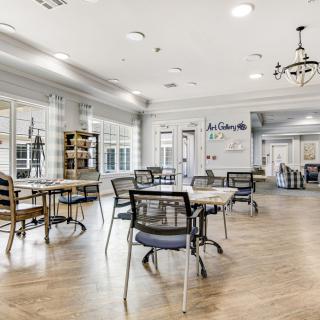 A cozy cafe interior with tables and chairs, featuring a chandelier and wooden flooring, bathed in bright lighting.
